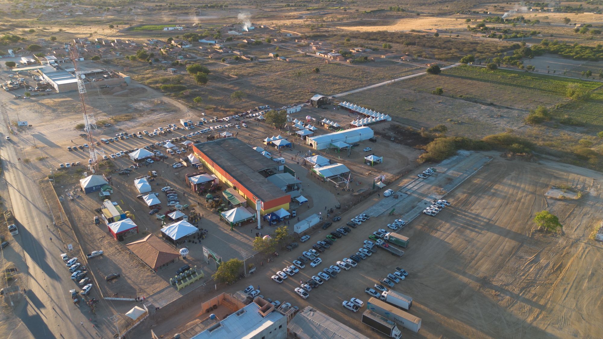 Vista aérea de uma dinâmica de campo: máquina na lavoura e público reunido sob tendas