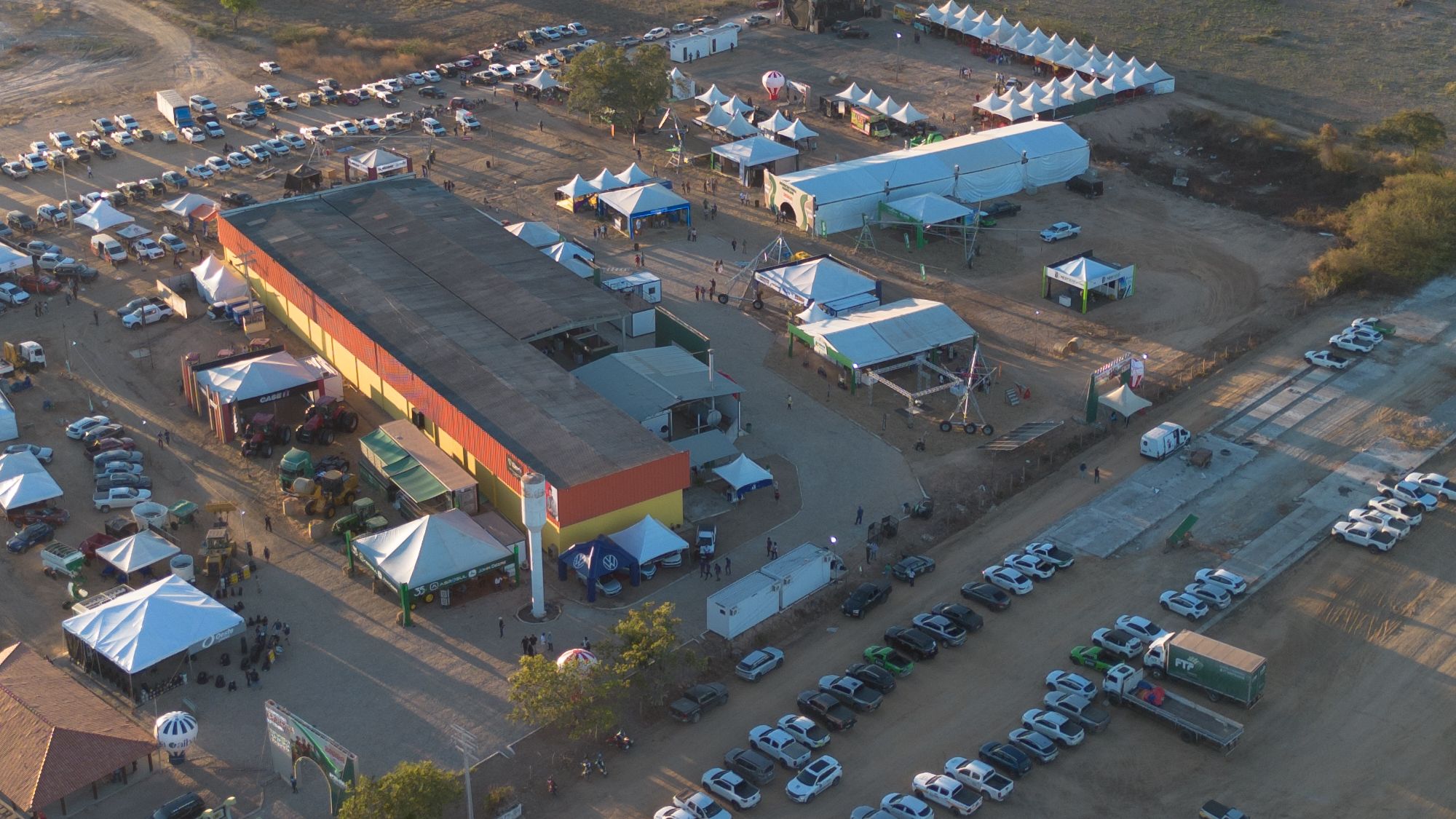 Vista aérea do pavilhão principal da feira com máquinas agrícolas expostas ao redor
