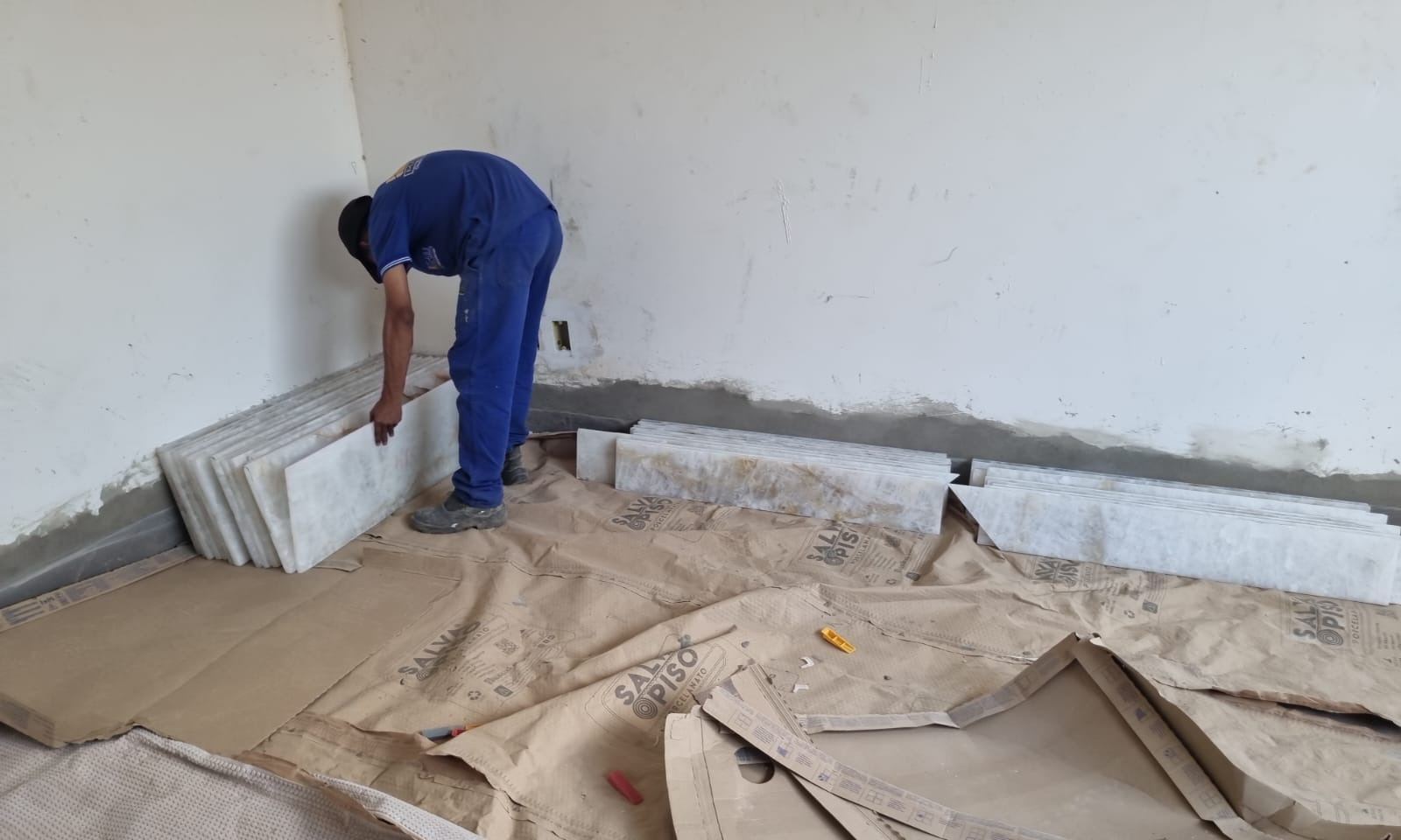 Profissional instalando rodapé de mármore com piso protegido