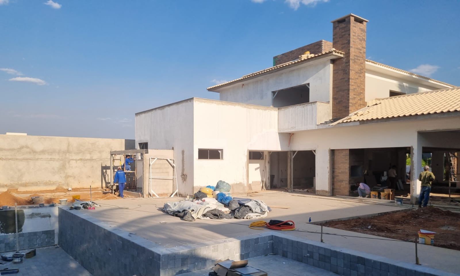 Piscina revestida e residência em fase de acabamento ao fundo